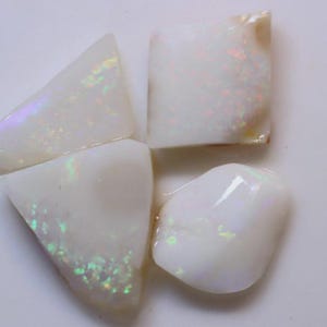 Peut inclure: Quatre pierres d'opale blanches avec des éclairs irisés de couleur. Les pierres sont taillées en formes irrégulières, dont des triangles et des formes arrondies. Les opales présentent une base blanc laiteux avec des reflets verts, bleus et roses.