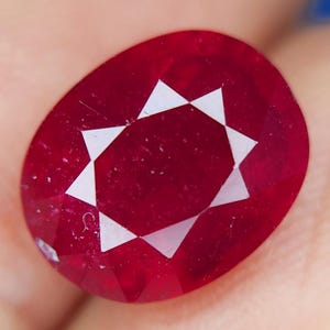 Può includere: Una pietra preziosa di rubino rosso intenso con un motivo a forma di stella al centro. Il rubino è tagliato a forma rotonda con sfaccettature.