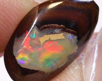 Puede incluir: Un cabujón de ópalo marrón oscuro y negro con un brillante destello iridiscente de rojo, verde y azul.