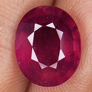 Può includere: Una pietra preziosa ovale di colore rosso scuro con taglio a faccette. La pietra preziosa ha un motivo a forma di stella al centro.