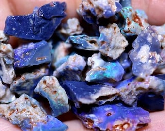 Puede incluir: Una colección de piedras preciosas de ópalo en bruto, azules y blancas. Los ópalos son de varios tamaños y formas, algunos muestran destellos iridiscentes de color.