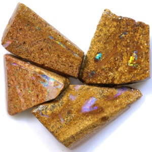 May include: Four rough-cut opal stones with a mix of tan, brown, and gold hues. The opals display iridescent flashes of blue, green, and yellow. The stones have a natural, textured appearance, showcasing their raw, uncut state.