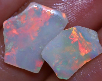 Puede incluir: Dos piezas de ópalo en bruto, una es gris claro con destellos naranja y rojo, la otra es gris claro con destellos verde y naranja.