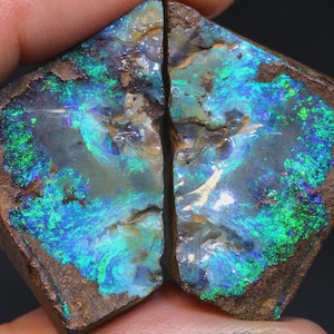 May include: Two pieces of rough opal, showcasing vibrant blue, green, and teal colors. The gemstone has a dark brown matrix surrounding the colorful interior, with a visible fracture line separating the two halves. The overall shape is roughly diamond-like.