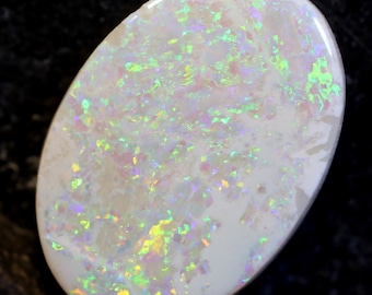 May include: A white opal cabochon with iridescent green, blue, and pink flashes. The opal has a smooth, polished surface and is oval shaped.