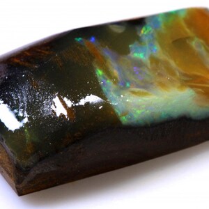 May include: A black opal gemstone with a dark brown matrix. The opal has a green, blue, and yellow iridescent sheen.