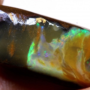 May include: A rough, dark brown, black, and green opal with iridescent flashes of color. The opal has a natural, unpolished finish.