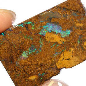 Puede incluir: Un ópalo en bruto de color marrón y dorado con destellos iridiscentes verdes y azules.