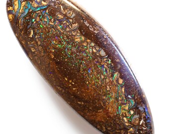 Puede incluir: Una gema pulida de forma ovalada con una base marrón oscura. La piedra presenta intrincados patrones de colores dorados, turquesas e iridiscentes. La gema se encuentra sobre un fondo blanco. La longitud de la piedra es de aproximadamente 5 cm.