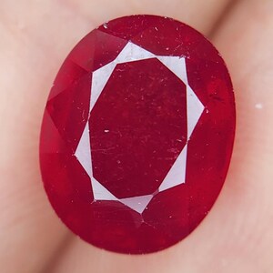 Può includere: Una pietra preziosa ovale di colore rosso scuro con taglio a faccette. La pietra preziosa ha una finitura lucida ed è incastonata in un anello.