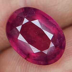 Può includere: Una pietra preziosa ovale di colore rosso intenso con taglio a faccette. La pietra preziosa ha un'alta lucidatura ed è incastonata in una montatura trasparente e chiara.