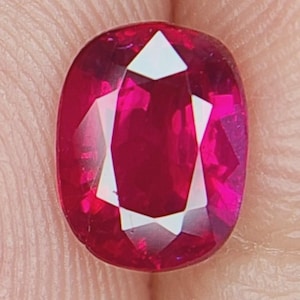 May include: A deep red oval-shaped ruby gemstone with a faceted cut.