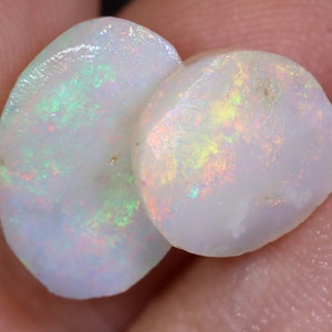 Op de afbeelding: Twee ovale witte opalen met iriserende regenboogkleuren. De opalen zijn glad en gepolijst.
