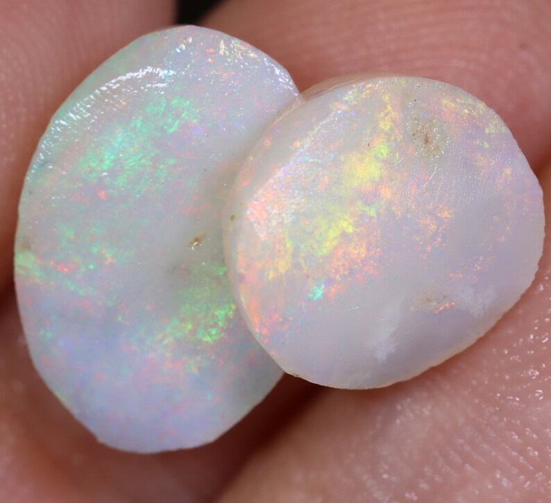 Op de afbeelding: Twee ovale witte opalen met iriserende regenboogkleuren. De opalen zijn glad en gepolijst.