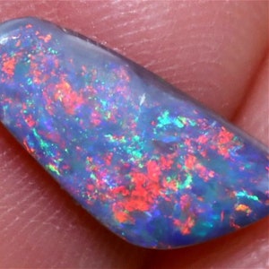 Könnte beinhalten: Nahaufnahme eines blauen Opals mit roten, grünen und blauen Farbschimmern. Der Opal ist ein roher, natürlicher Stein mit einer glatten, polierten Oberfläche.