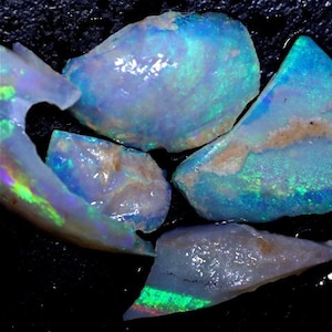 Könnte beinhalten: Eine Sammlung von fünf rohen Opal-Steinen mit schillernden blauen, grünen und violetten Farbtönen. Die Steine sind in verschiedenen Größen und Formen.