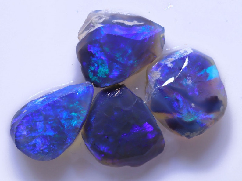 K&ouml;nnte beinhalten: Vier rohe blaue Opale mit schillernden Farbflecken. Die Opale sind in verschiedenen Gr&ouml;&szlig;en und Formen.