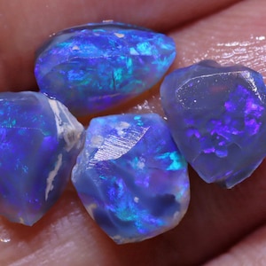 K&ouml;nnte beinhalten: Eine Gruppe von f&uuml;nf rohen blauen Opal-Steinen mit schillernden Farbflecken. Die Steine sind in verschiedenen Formen und Gr&ouml;&szlig;en.