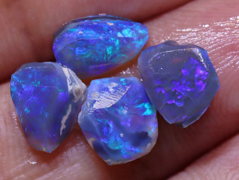 K&ouml;nnte beinhalten: Eine Gruppe von f&uuml;nf rohen blauen Opal-Steinen mit schillernden Farbflecken. Die Steine sind in verschiedenen Formen und Gr&ouml;&szlig;en.