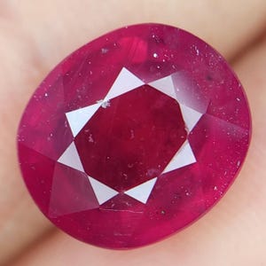 May include: A deep red oval-shaped gemstone with a faceted cut and a star-shaped pattern.