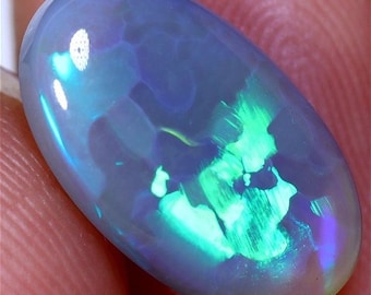 May include: A blue-green opal gemstone with a swirling pattern of color. The opal is oval shaped and has a smooth, polished surface.
