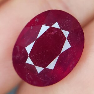 Può includere: Una pietra preziosa ovale di colore rosso intenso con taglio a faccette e un motivo a forma di stella.