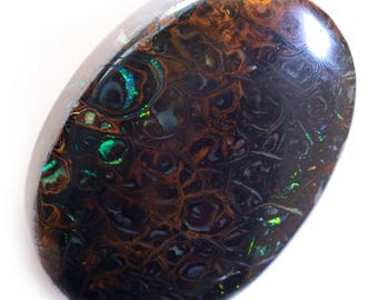 Puede incluir: Una piedra preciosa de ópalo ovalada de color marrón oscuro con destellos iridiscentes verdes y azules. El ópalo tiene una superficie texturizada y un alto pulido.
