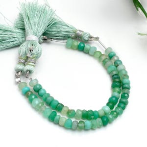Op de afbeelding: Twee strengen groene edelsteen kralen in verschillende groentinten worden getoond. De kralen zijn aan elkaar geregen en een mintgroene kwast is aan de bovenkant bevestigd. De kralen zijn gefacetteerd en hebben een gepolijste afwerking.