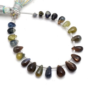 Puede incluir: Un collar de piedras preciosas en forma de lágrima en tonos azules, verdes y marrones. Las cuentas están ensartadas en un alambre de plata, con una borla decorativa en la parte superior. Las piedras preciosas tienen una superficie pulida y lisa.