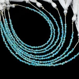 May include: Several strands of light blue opal beads with a pearlescent sheen. Each strand is composed of small, oval-shaped beads. White tassels are attached to the top of each strand. The background is solid black.