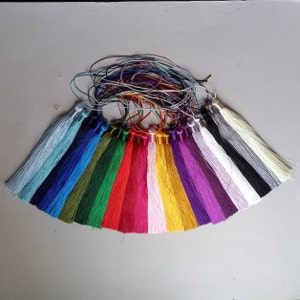 May include: A collection of colorful tassels in various shades, including blue, green, red, pink, yellow, and purple. Each tassel has a metallic cap and is attached to a thin cord. The tassels are arranged in a fan shape.