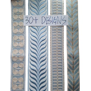 Peut inclure: Quatre bandes verticales de galons décoratifs présentant divers motifs brodés dans des tons bleu clair, crème et blanc. Une étiquette rectangulaire blanche avec le texte manuscrit 30+ DESIGNS est placée au centre des bandes.