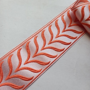 May include: Orange embroidered trim with a white background. The trim features a repeating pattern of stylized leaves.