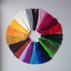 Könnte beinhalten: Ein Set mit 15 bunten Quasten, die in einem Kreis angeordnet sind. Die Quasten bestehen aus einem weichen, seidenartigen Material und sind in verschiedenen Farben erhältlich, darunter Rot, Orange, Gelb, Grün, Blau, Lila und Weiß.