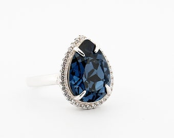 May include: A silver ring with a large, dark blue pear-shaped gemstone surrounded by a halo of smaller clear gemstones.