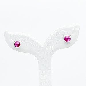 Può includere: Un paio di orecchini a perno d'argento con piccoli strass rosa.