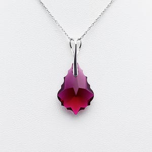 Peut inclure: Un collier en argent avec un pendentif facetté en forme de goutte, de couleur magenta foncé et rouge rubis. Le pendentif est suspendu à une fine chaîne en argent, contrastant avec le fond blanc. La coupe du pendentif met en valeur son éclat.