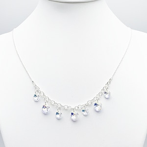 Puede incluir: Un collar de cadena de plata con gotas de cristal colgantes. Los cristales son transparentes y tienen un ligero brillo iridiscente.