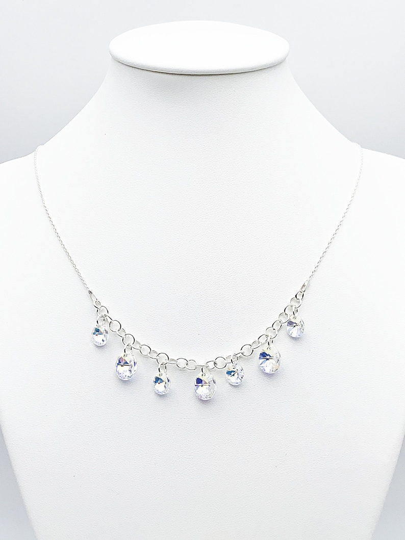 Puede incluir: Un collar de cadena de plata con gotas de cristal colgantes. Los cristales son transparentes y tienen un ligero brillo iridiscente.