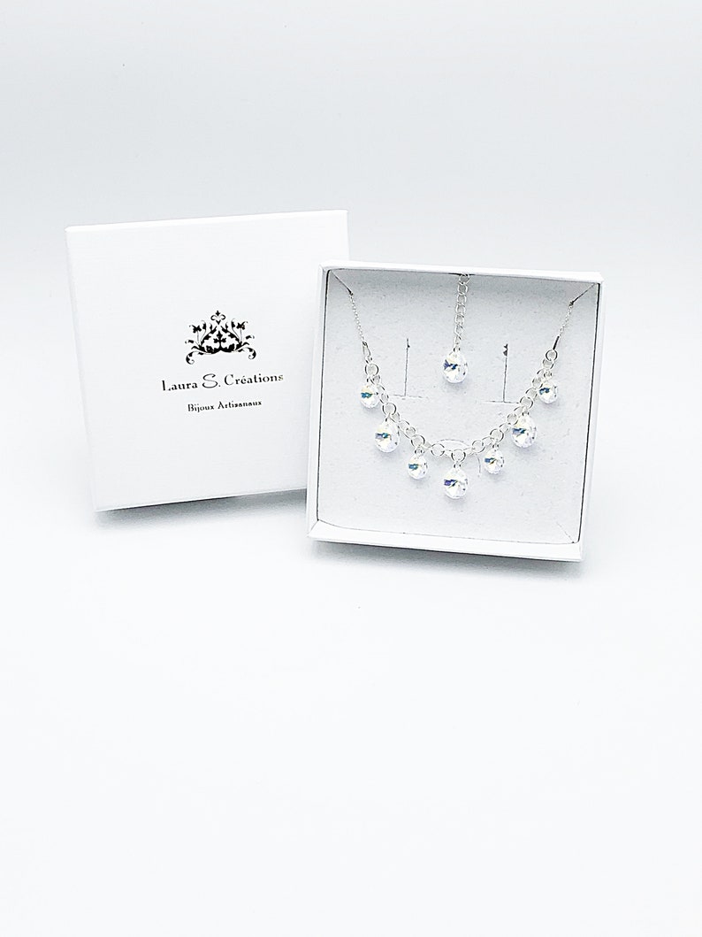Puede incluir: Un conjunto de collar y pendientes de plata con piedras de cristal transparentes. Las joyas est&aacute;n empaquetadas en una caja blanca con el texto "Laura S. Creations Bijoux Artisanais".