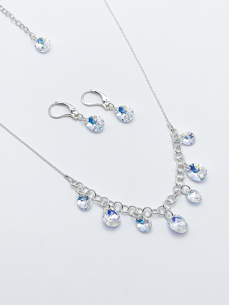 Puede incluir: Un collar de plata con una cadena delicada y gotas de cristal colgantes. Se incluyen pendientes de cristal a juego con ganchos de plata.