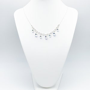Puede incluir: Un collar de cadena de plata con gotas de cristal transparente que cuelgan de &eacute;l. El collar se muestra en un busto de maniqu&iacute; blanco.