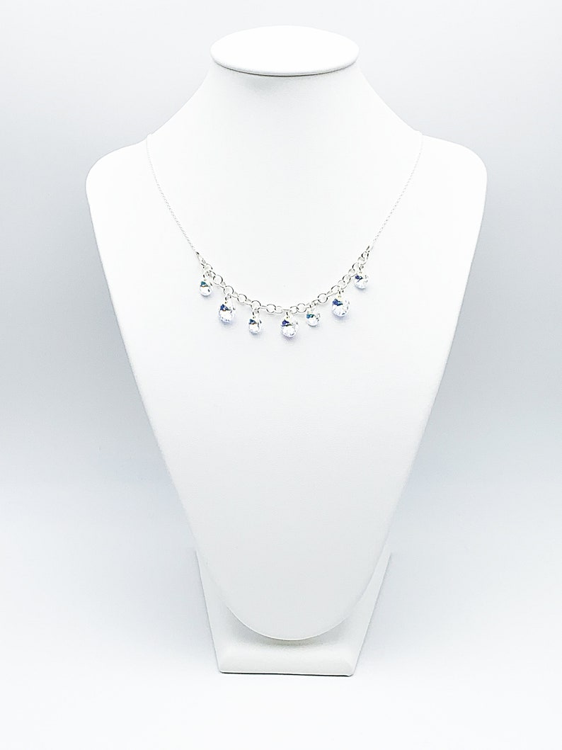 Puede incluir: Un collar de cadena de plata con gotas de cristal transparente que cuelgan de &eacute;l. El collar se muestra en un busto de maniqu&iacute; blanco.