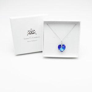 May include: A silver necklace with a blue crystal heart pendant in a white box. The box has the text "Laura & Cr&eacute;ations Bijoux Artisanaux" printed on it.