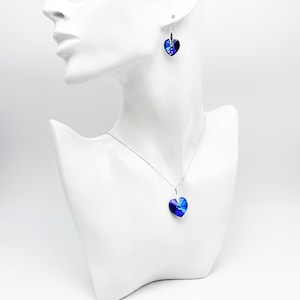 May include: A silver necklace and earrings set with a blue heart-shaped crystal pendant and matching earrings.