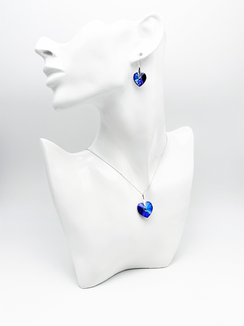 May include: A silver necklace and earrings set with a blue heart-shaped crystal pendant and matching earrings.