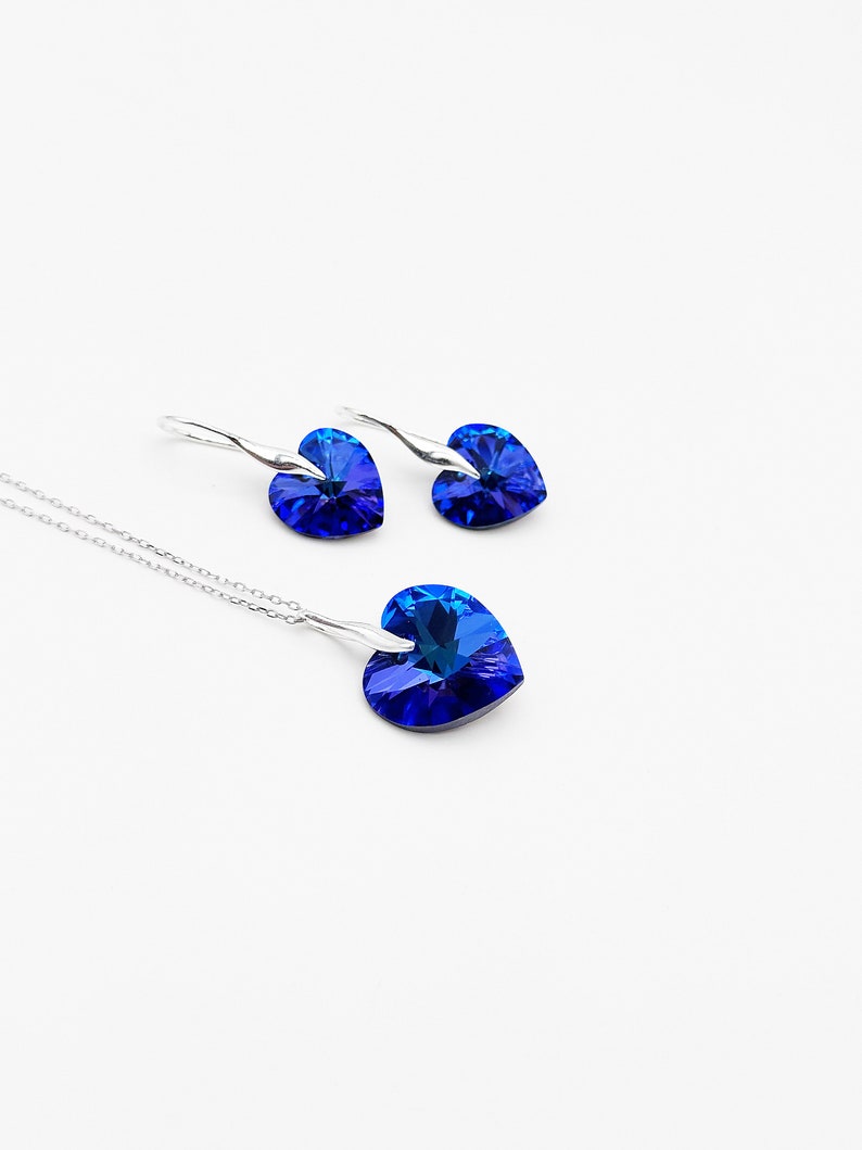 May include: A silver necklace and earrings set with a blue heart-shaped crystal pendant and matching earrings.