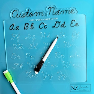 May include: A clear acrylic cursive writing board with the text "Custom Name" and "Learn to Write - Cursive Letters". The board features the alphabet in cursive, with a black marker and a green eraser marker. The background is a light blue.