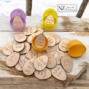 May include: Wooden egg-shaped tokens with various activities and rewards written on them, such as "Movie Night", "Extra Screen Time", "Lunch Date", and "50 Cents". The tokens are scattered on a wooden surface with two plastic Easter egg containers, one purple and one yellow, with the words "$5" and "Playtime at the" written on the inside.