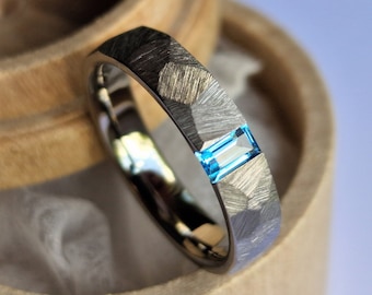 Faceted titanium tension ring with baguette cut stone setting.
